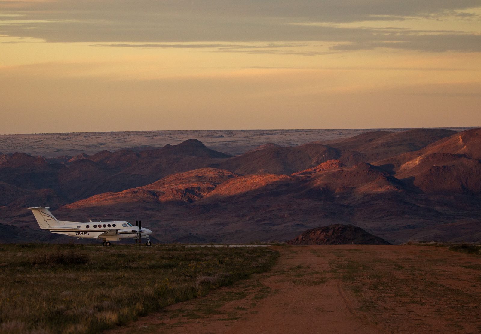 Light aircraft on a dirt airstrip at dusk, with mountain ranges behind